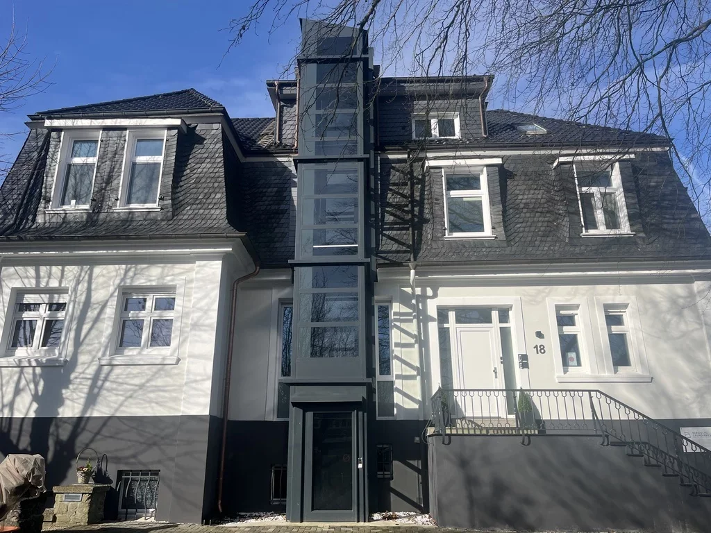 Au&szlig;enliegender Aufzugsschacht mit dunkler Verglasung an der Fassade eines Altbaus