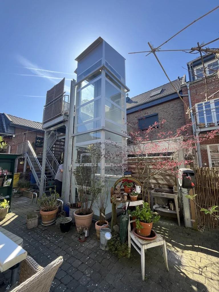 Gl&auml;serner Aufzugsschacht im Innenhof eines Altbaus mit Garten