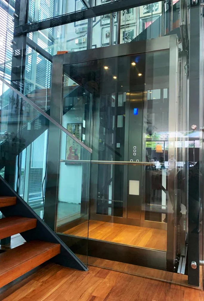 Verglaster Personenaufzug neben einer Holztreppe in einem modernen Treppenhaus