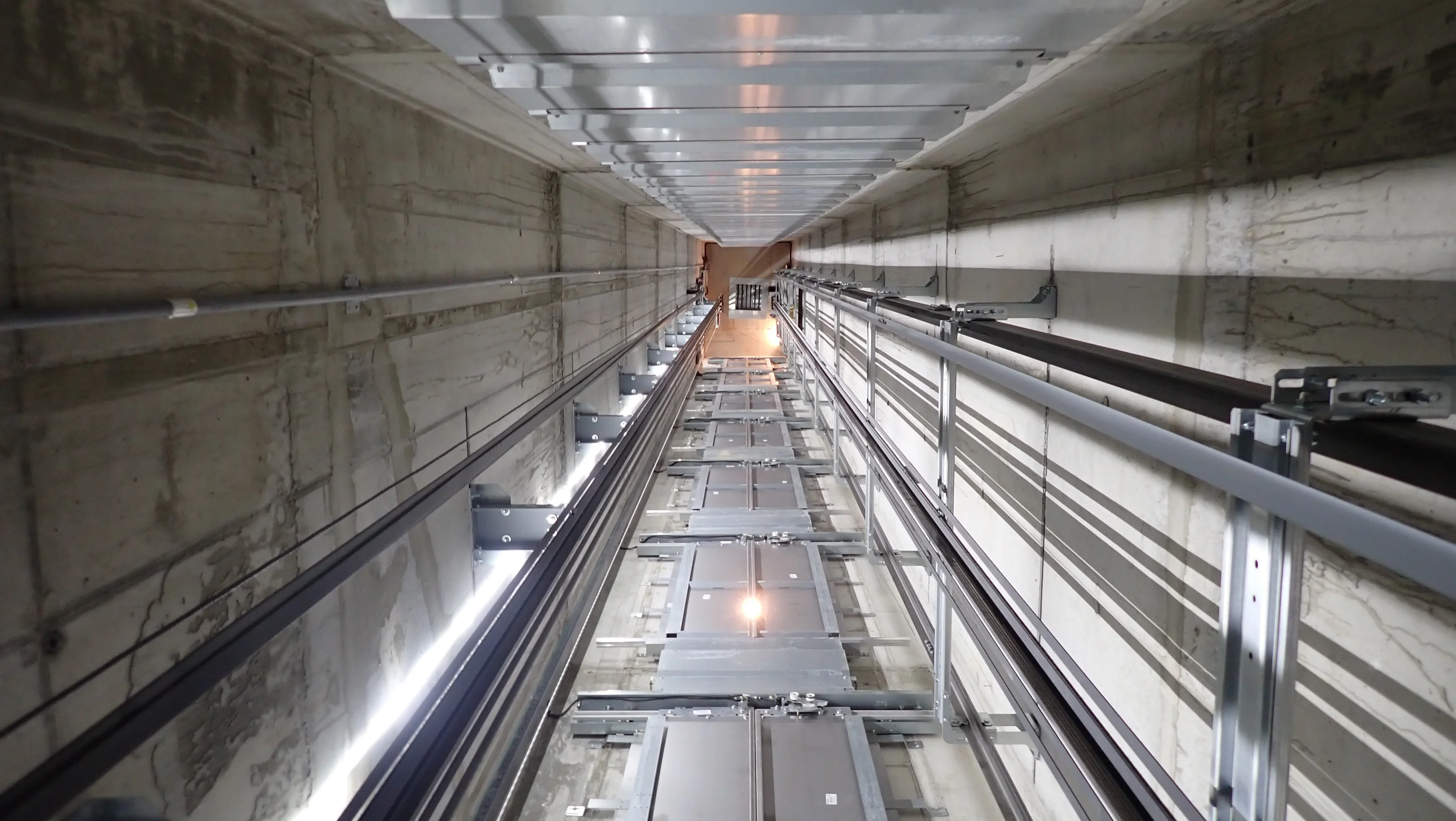 Blick in einen Aufzugsschacht aus Beton mit F&uuml;hrungsschienen und Beleuchtung