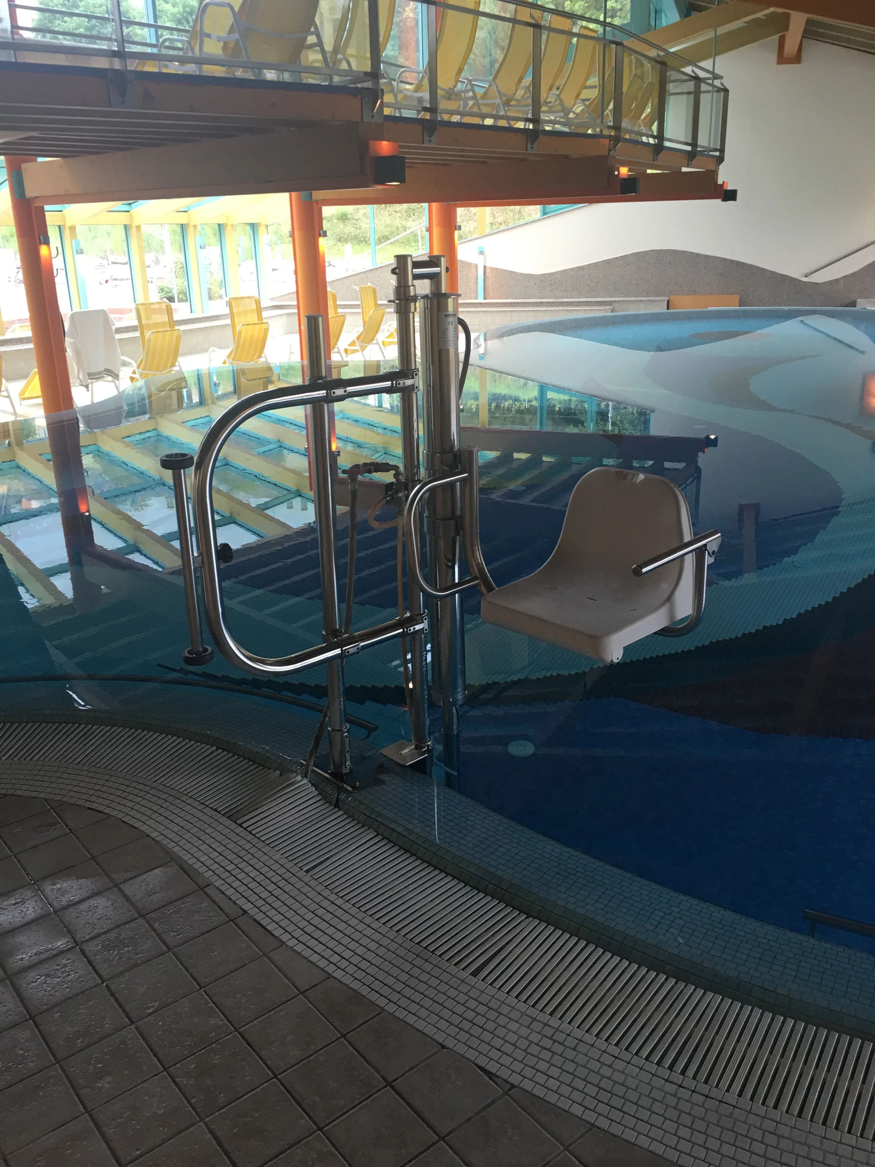 Poollift mit wei&szlig;em Sitz am Beckenrand eines Hallenbads