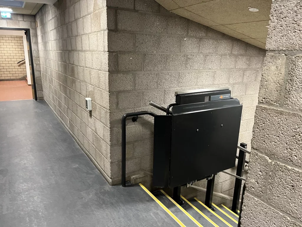 Zusammengeklappter Plattformlift in Schwarz am Fu&szlig; einer Treppe im Flur