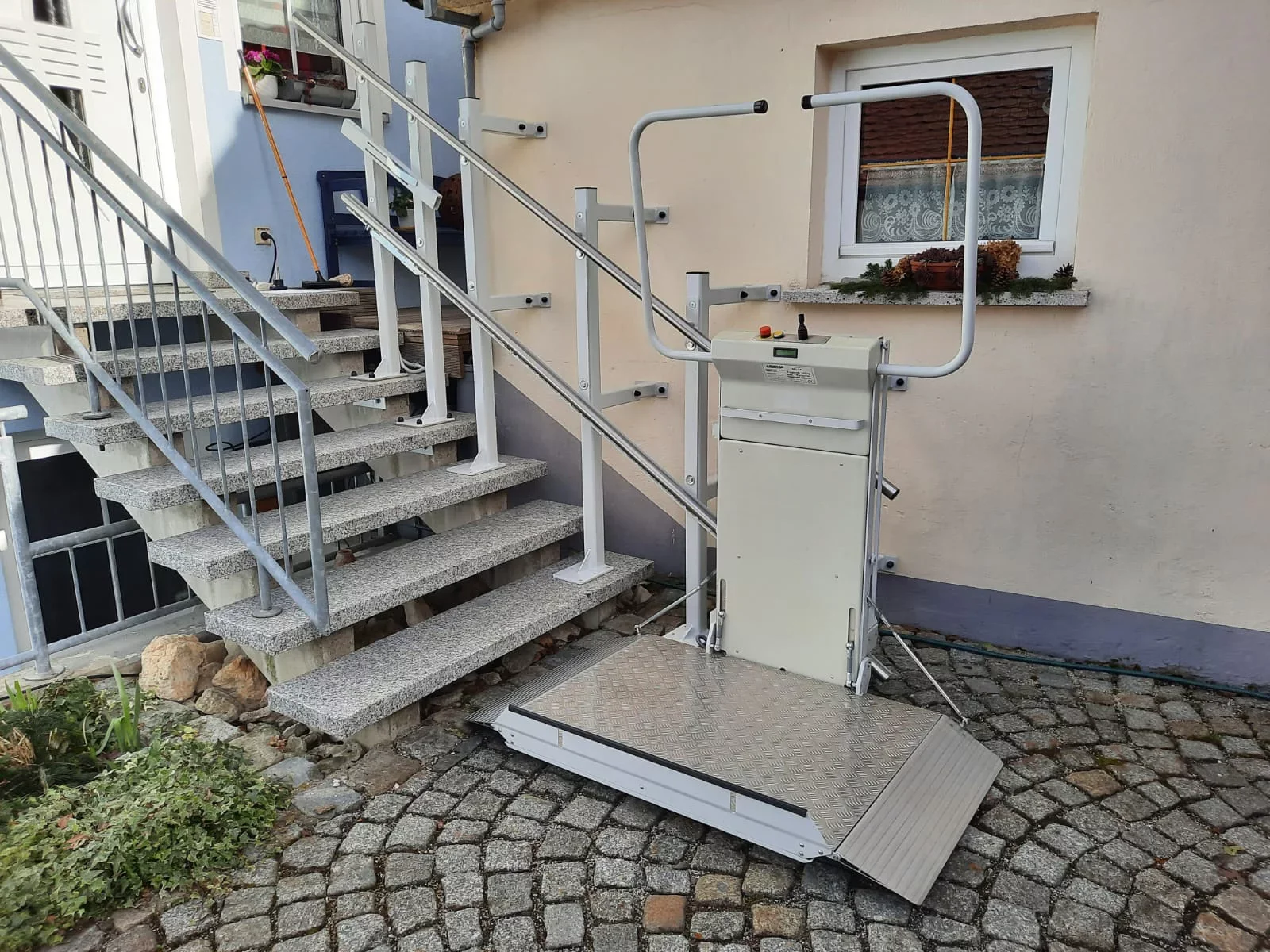 Rollstuhllift mit ausgeklappter Plattform an der Au&szlig;entreppe eines Wohnhauses