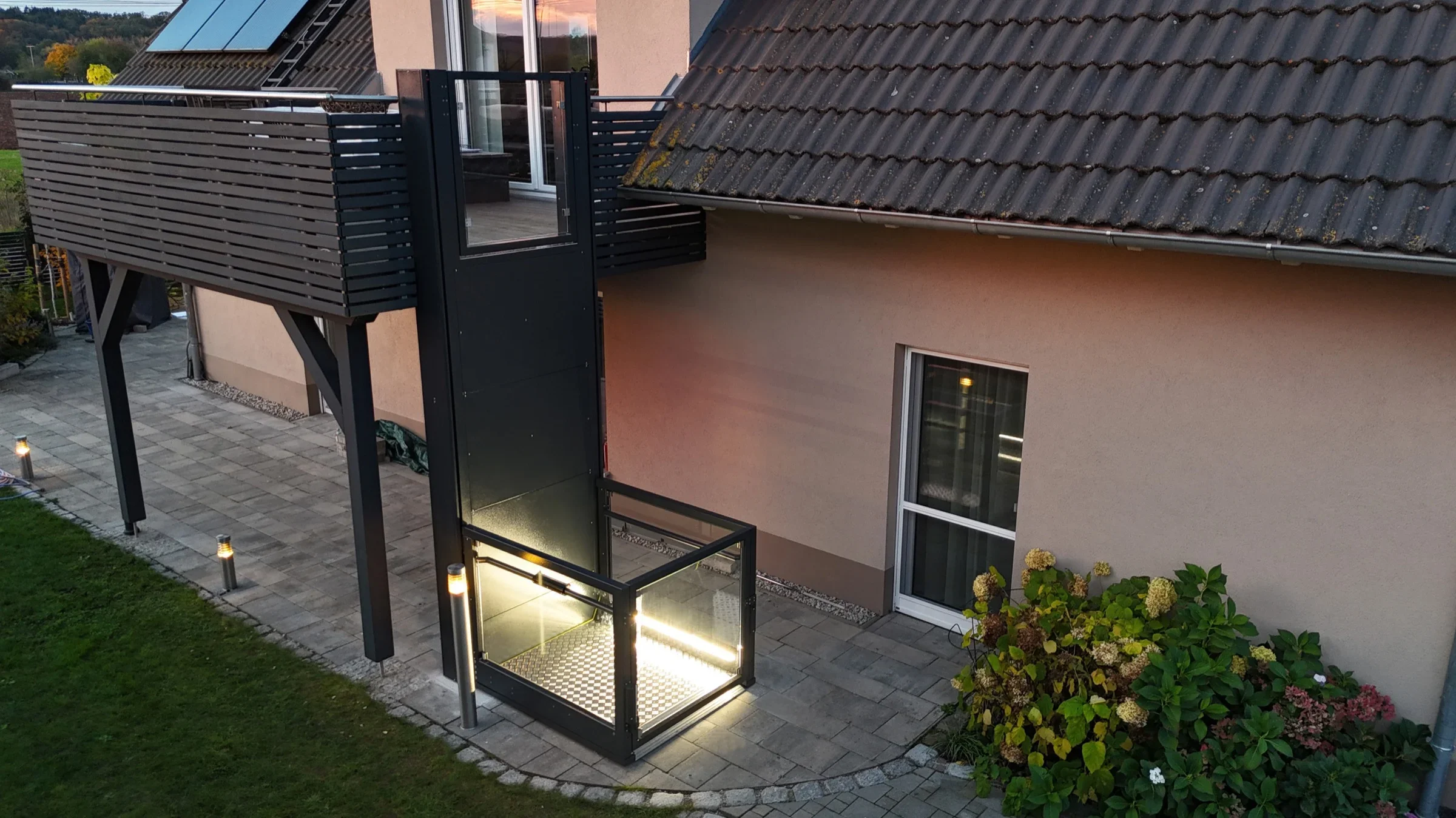 Beleuchteter Plattformlift RB150 am Balkon eines Einfamilienhauses in der Abendd&auml;mmerung