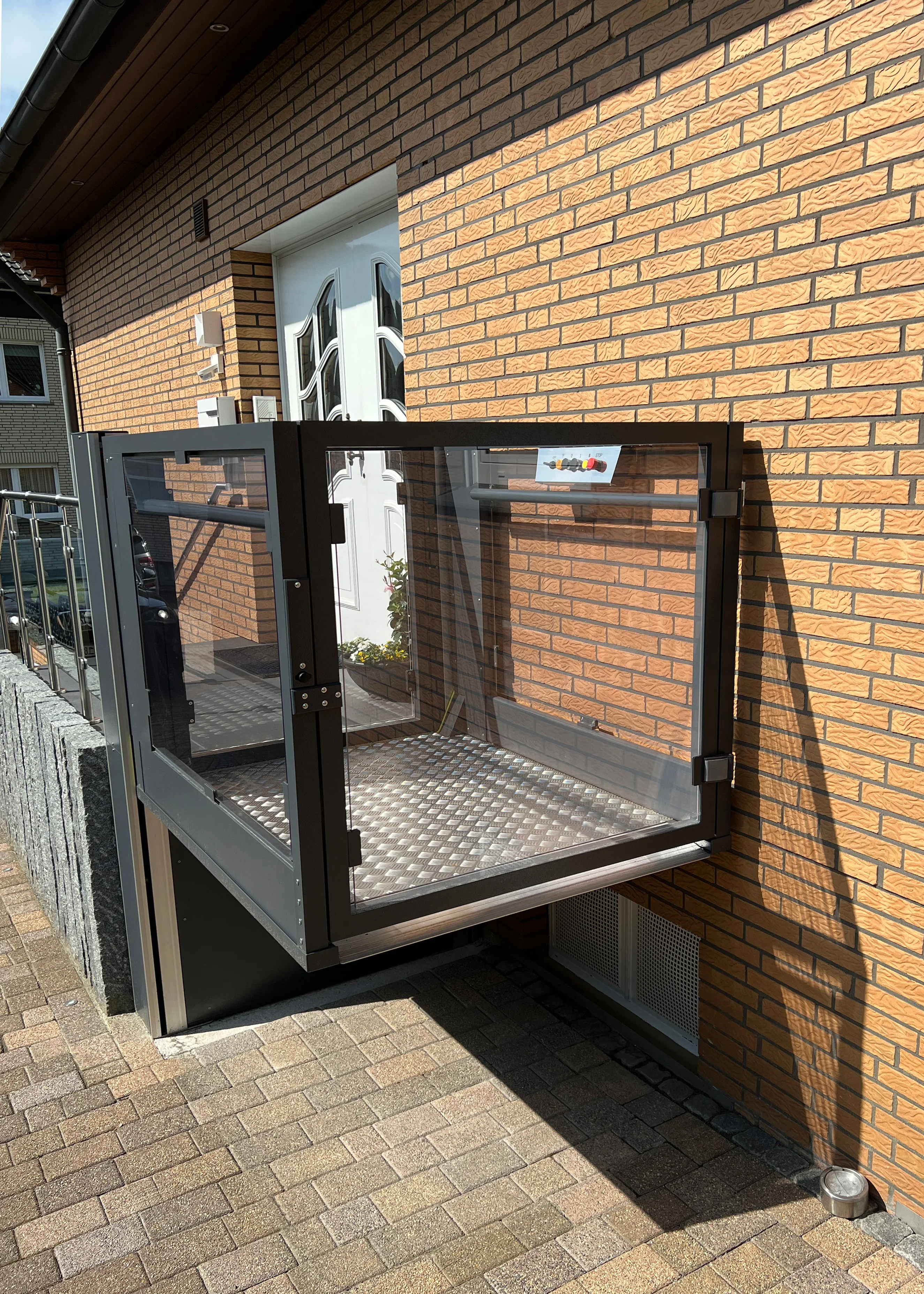 Vertikaler Plattformlift an einer Klinkerfassade am Hauseingang