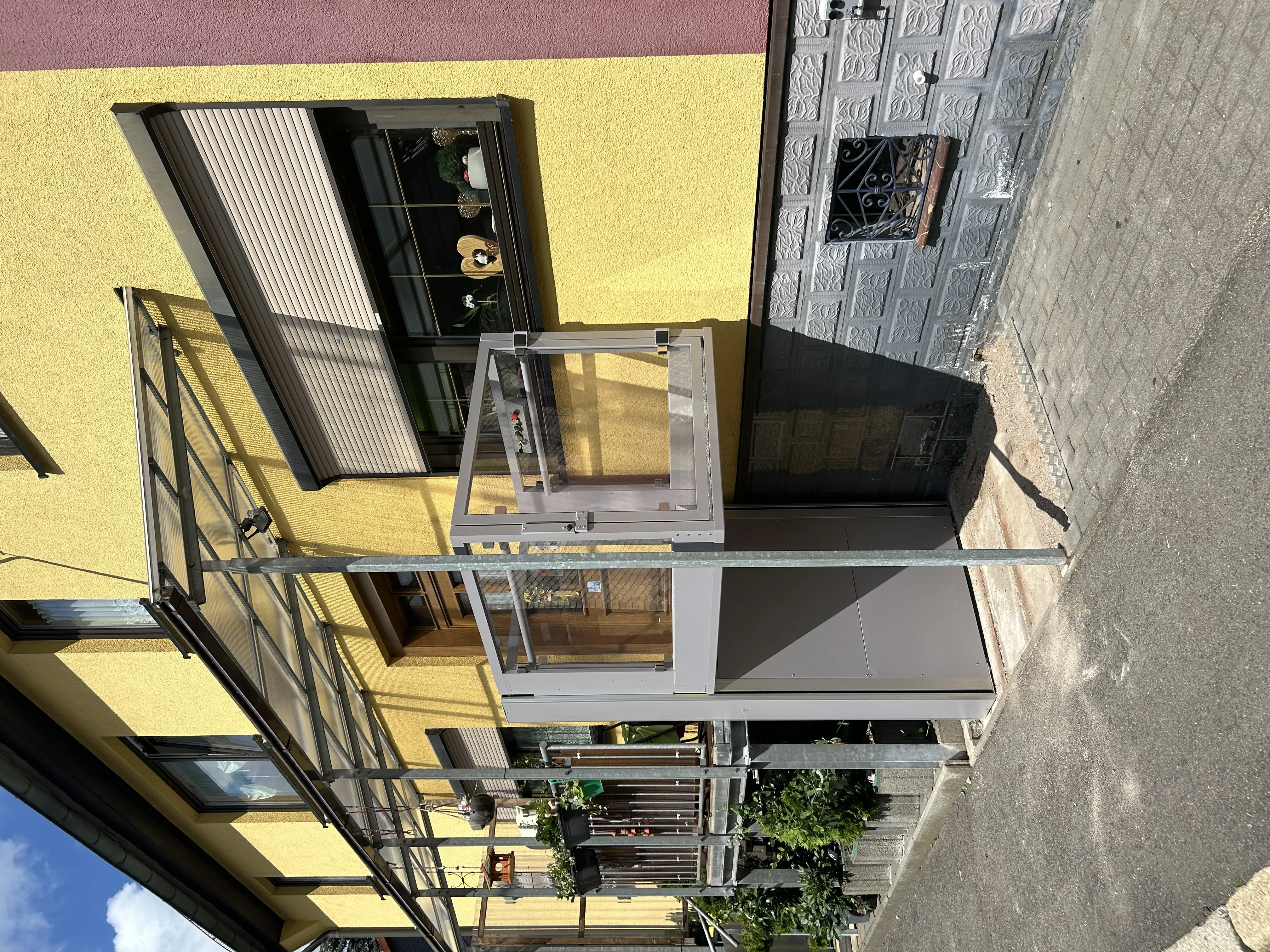 Vertikaler Plattformlift an einer gelben Hausfassade, Blick von oben