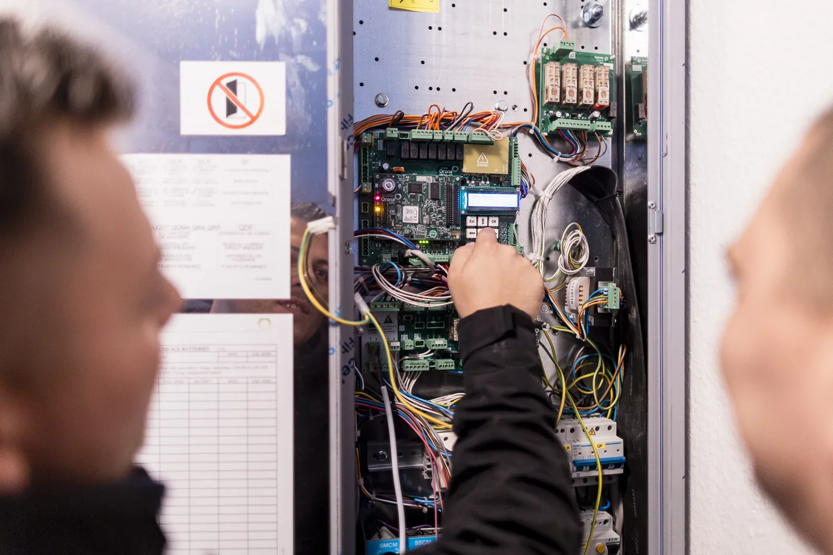 Zwei Techniker von ALPHA Aufzugsservice an einem ge&ouml;ffneten Steuerschrank