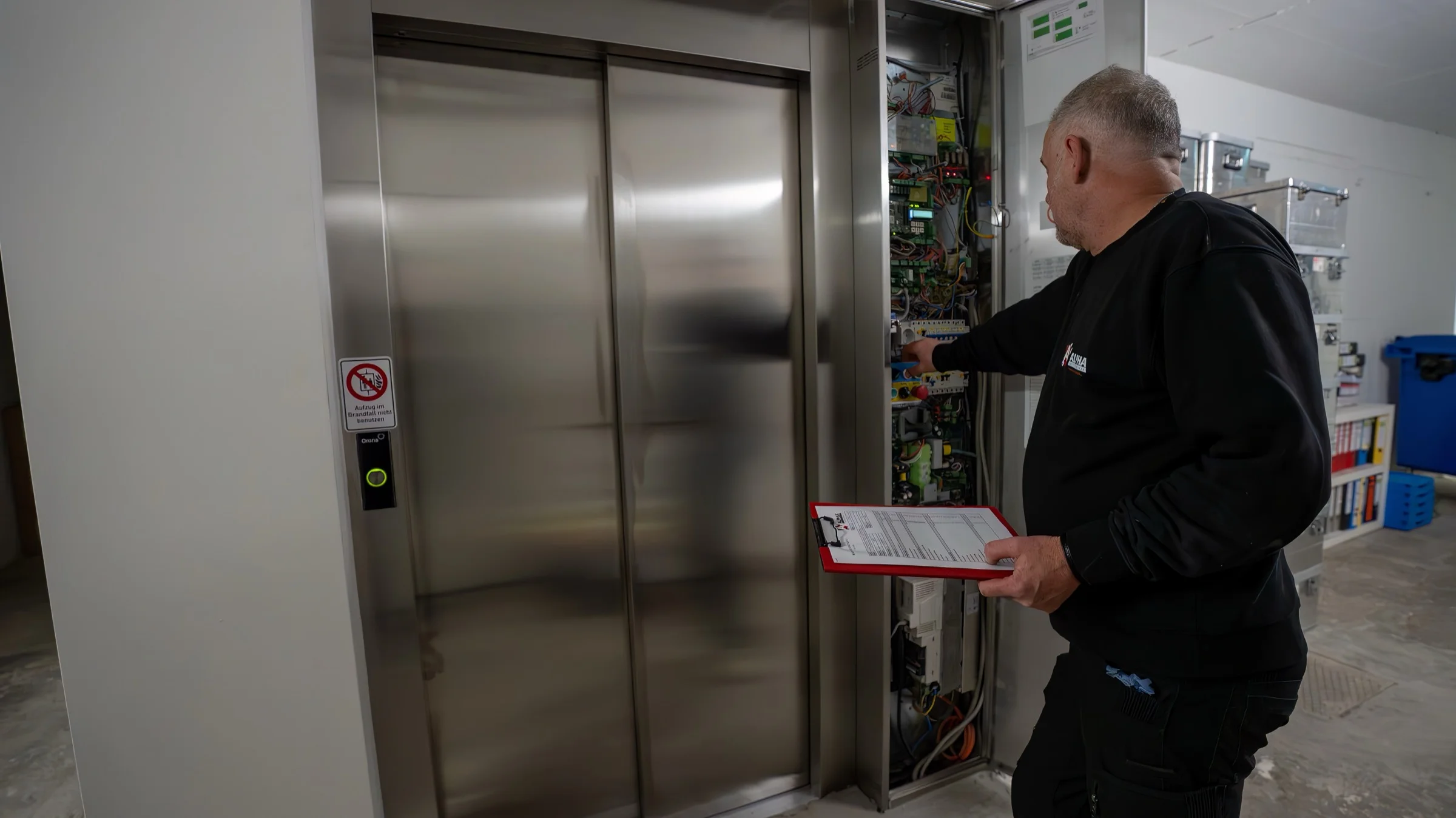 Servicetechniker mit Checkliste am geöffneten Steuerschrank neben einer Aufzugstür